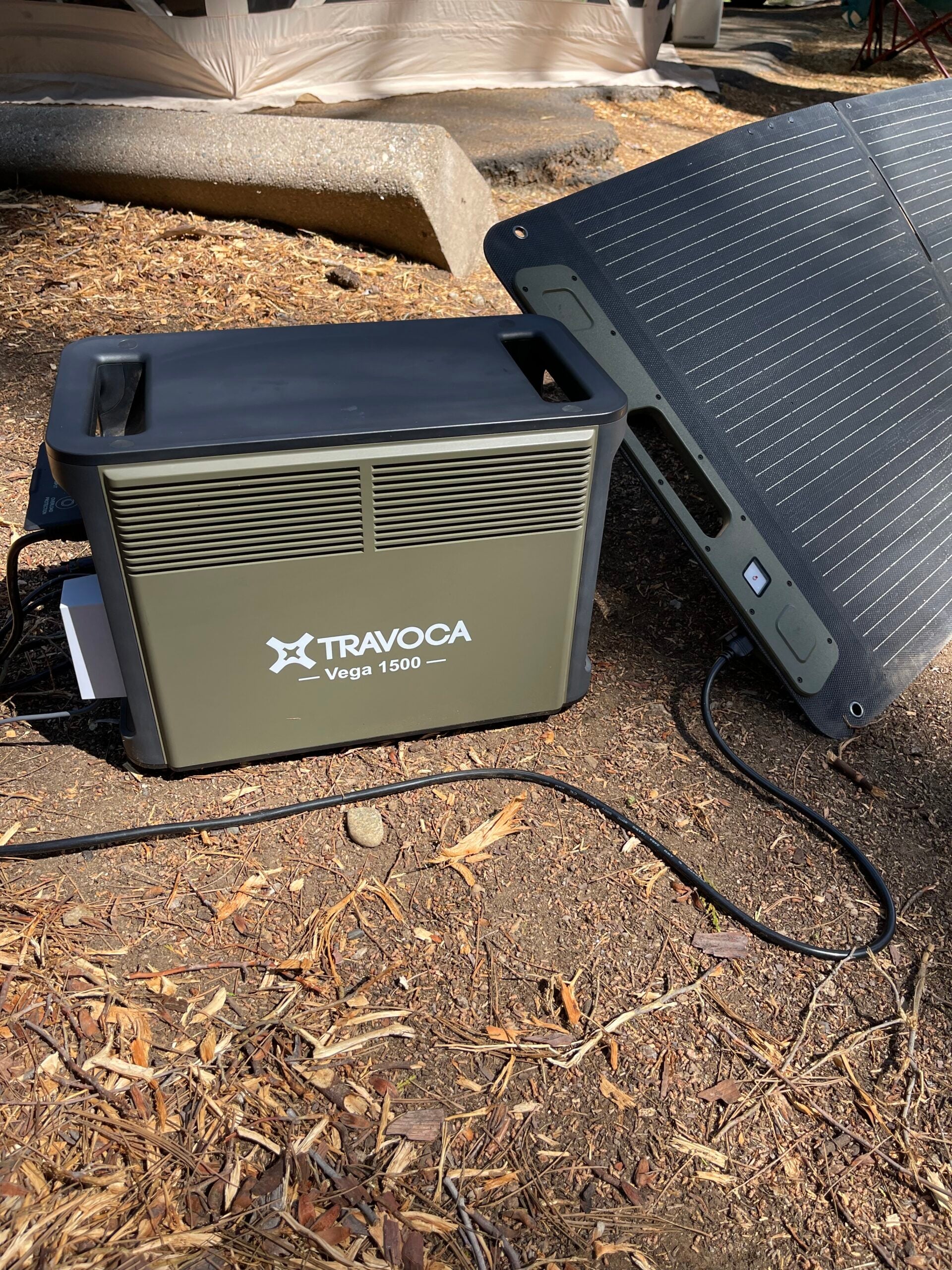 TRAVOCA Vega 1500 portable power station connected to Vega Sol 200 solar panel in an outdoor camping setup for off-grid power supply.